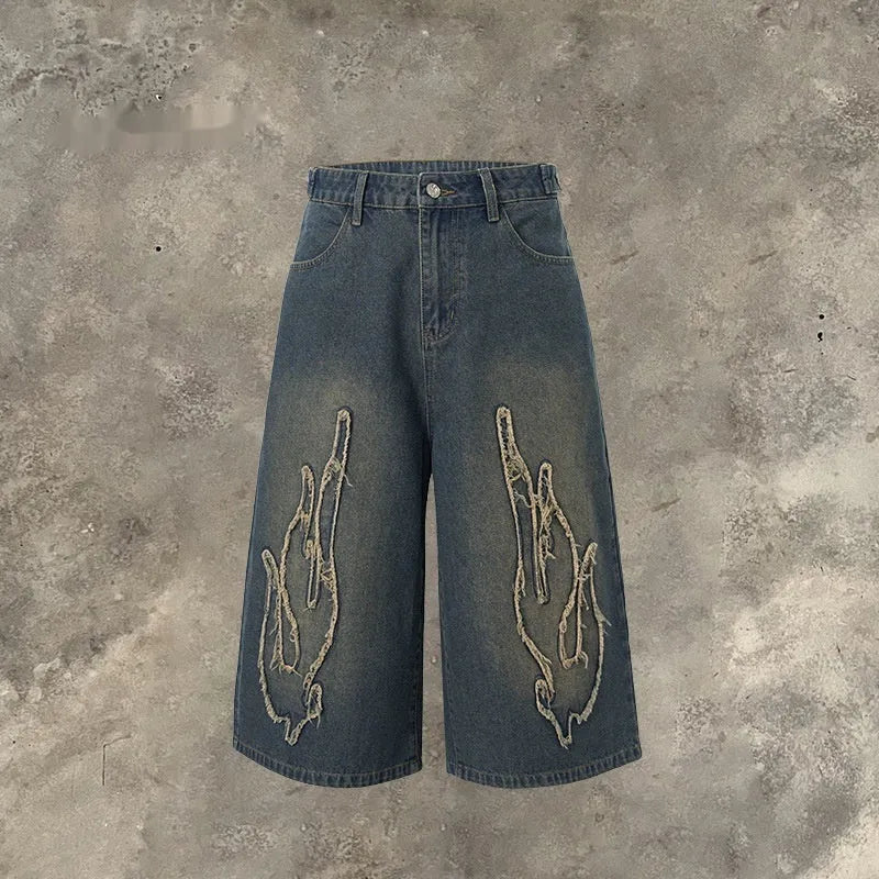 Men's black denim shorts with a cropped flame embroidery patch on the leg.