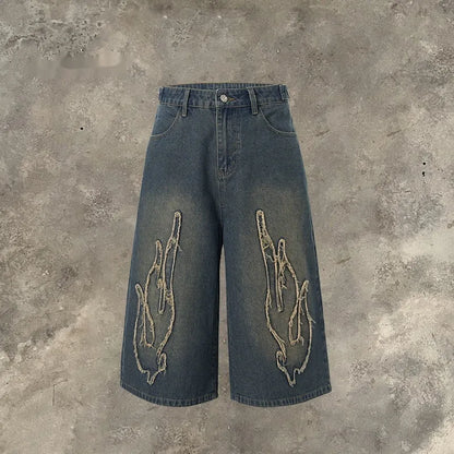 Men's black denim shorts with a cropped flame embroidery patch on the leg.