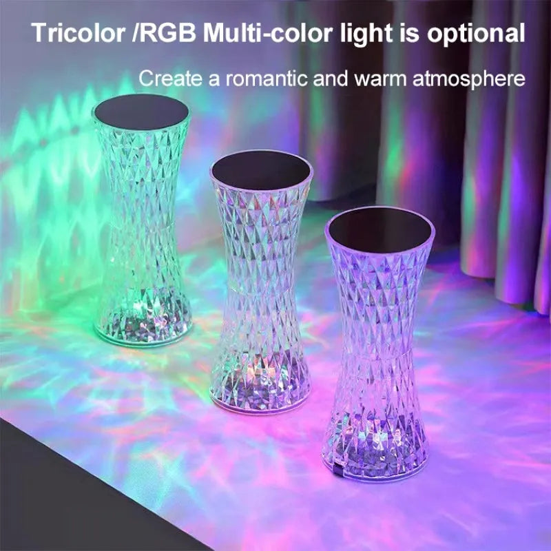 Transparent vase-shaped crystal table lamp with remote control on a wooden bedside table.