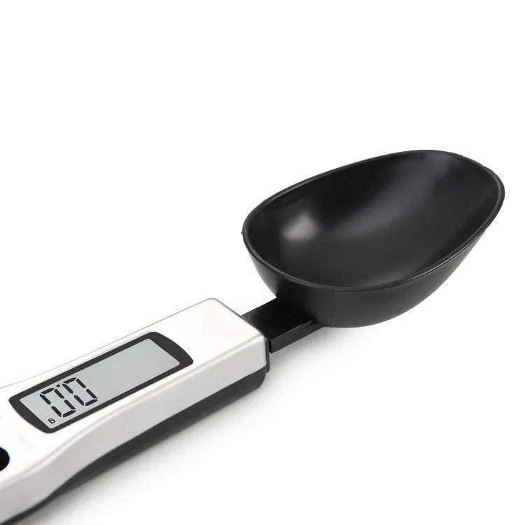 Smart digital measuring spoon with electronic display showing weight, alongside two AAA batteries.