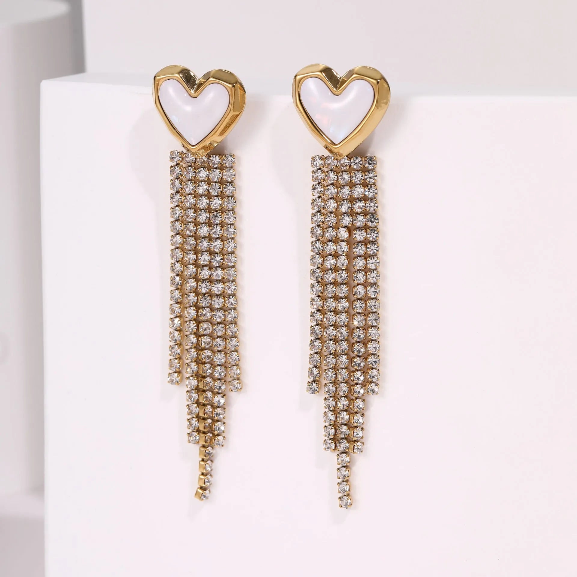 Gold-coloured women's earrings with a love heart shape, star details and dangling diamond-style tassels on a white background.