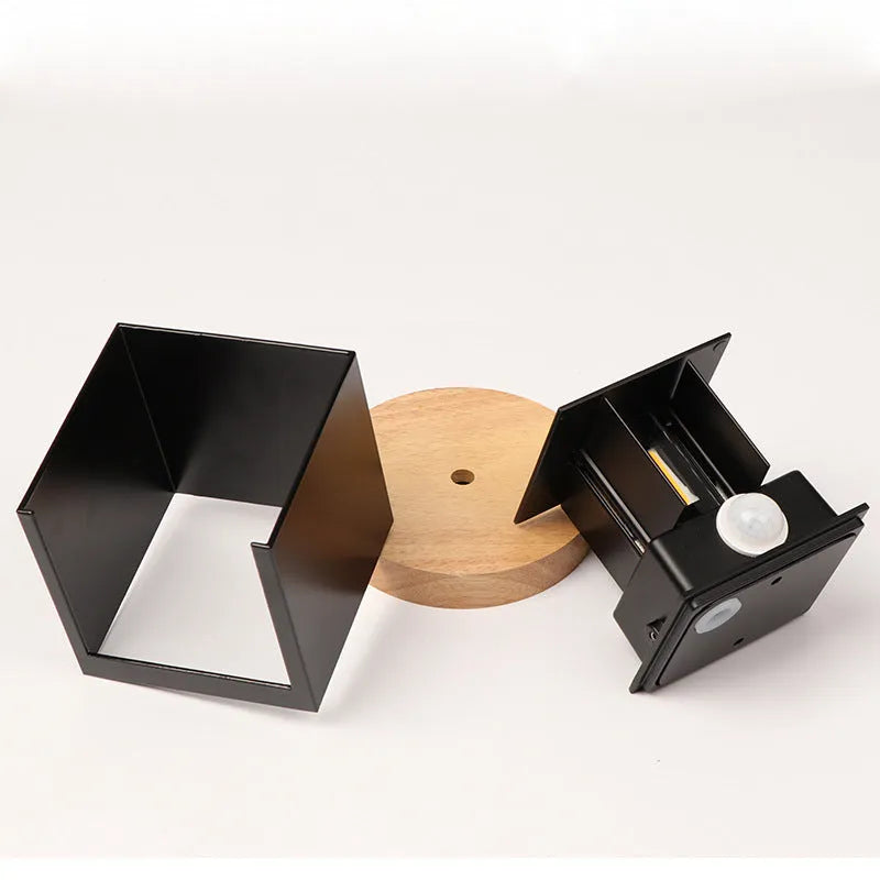 Modern cubic wall lamp in black finish mounted on a corridor wall, emitting a warm white light.