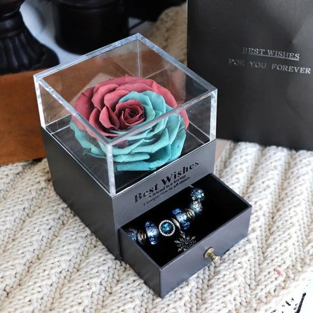 Blue and pink eternal flower gift box with roses and carnations on a table.