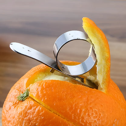 Silver stainless steel citrus fruit peeler with a ring handle on a wooden surface.