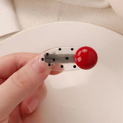 Red plastic hair clip with a 3D love heart and dots on a willow leaf-shaped base.