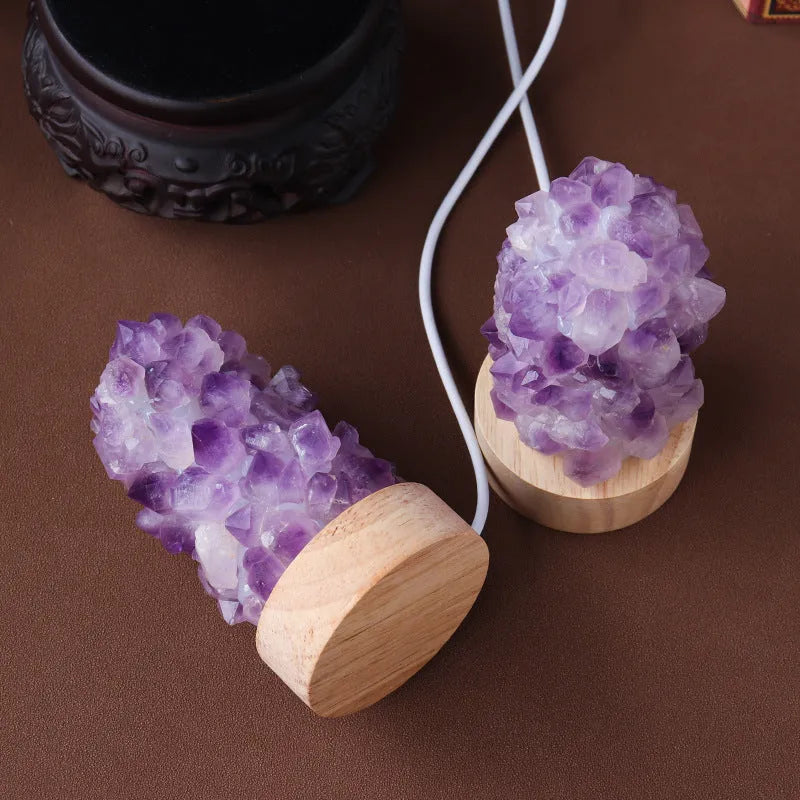 Miniature amethyst crystal tooth flower night light glowing with warm light on a wooden surface.