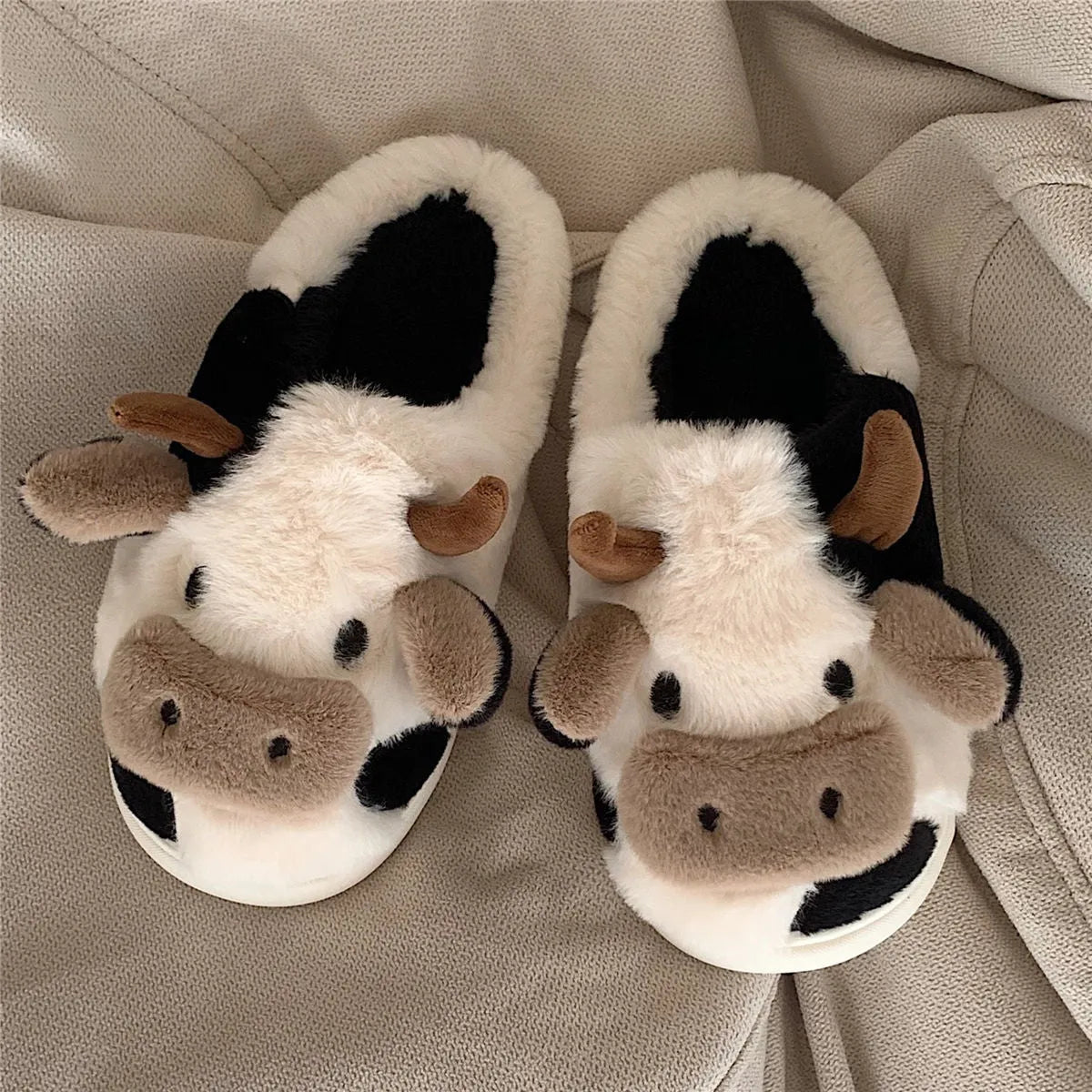 White cow-themed plush slippers with a non-slip textured sole for women.