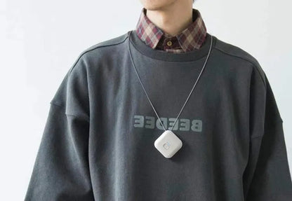 Pink wearable USB air purifier necklace on a table with USB cable, showing compact size.