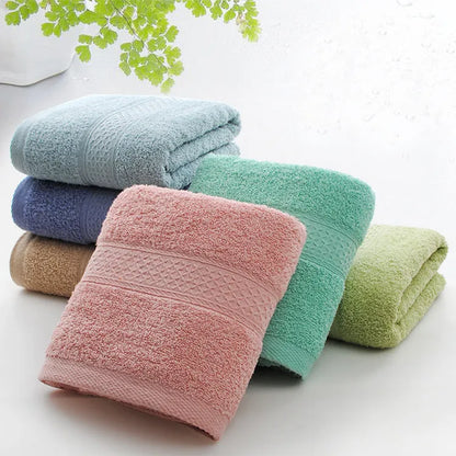 A stack of thickened cotton bath and beach towels in various colours including apple green, dark blue, and light pink.