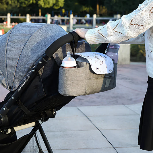 Baby stroller organiser with cup holder mounted on pram pole showing storage compartments