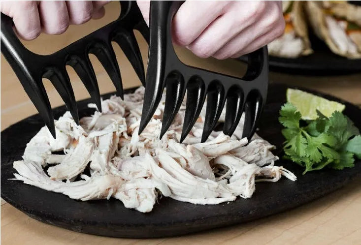 Two black bear claw meat shredders with decorative handles on a kitchen surface.