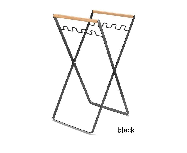 Black iron folding trash rack with wooden handles mounted on a wall holding a recycling bag.