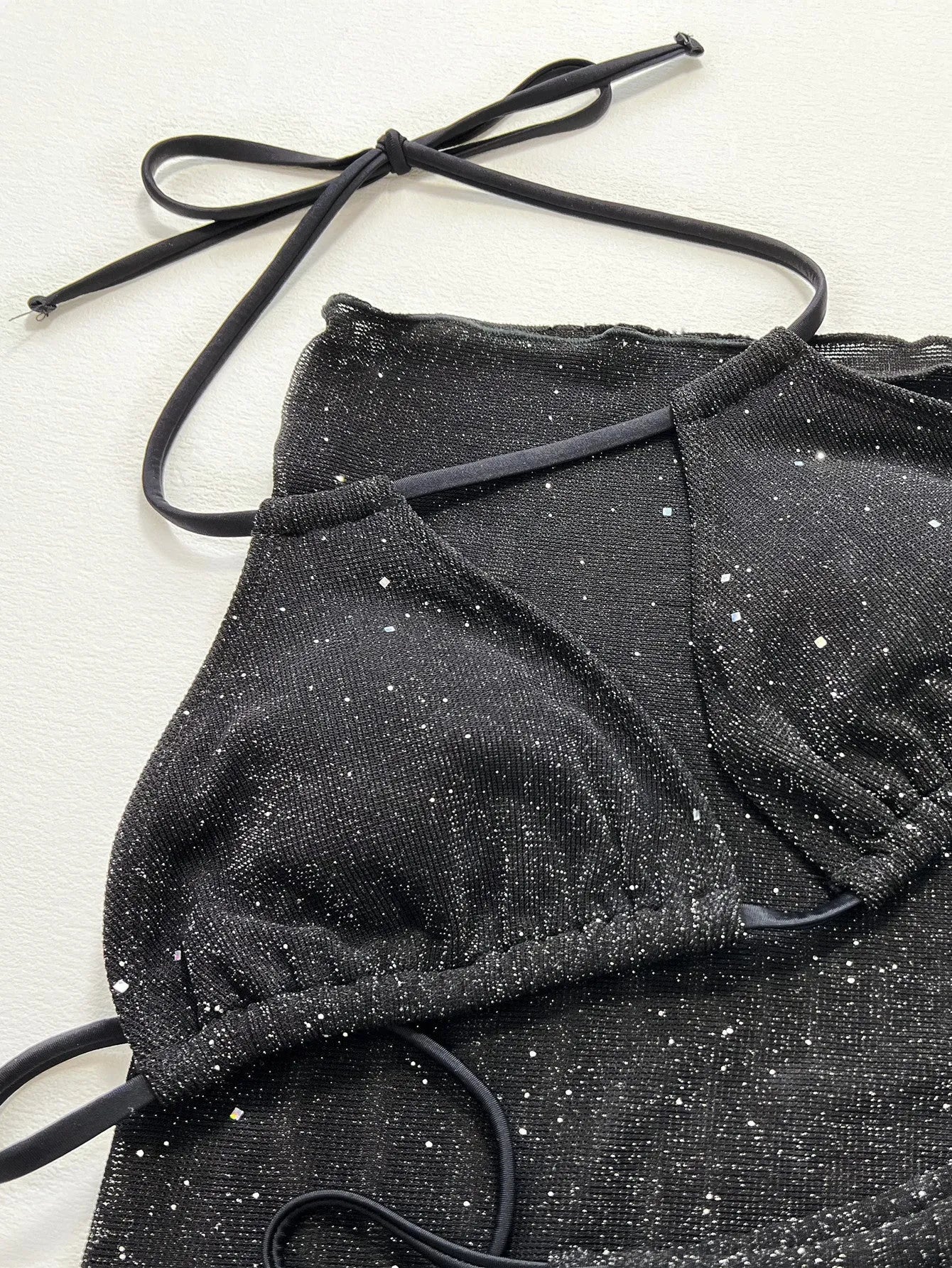 Black three-piece swimsuit bikini set with a top and shorts laid flat.