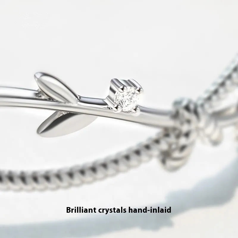 Close-up of a white gold coloured twisted copper bracelet with a branch and sprout design.
