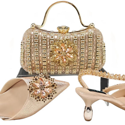 Women's black high-heel ankle strap shoes with floral rhinestone buckle and matching clutch bag on a neutral background