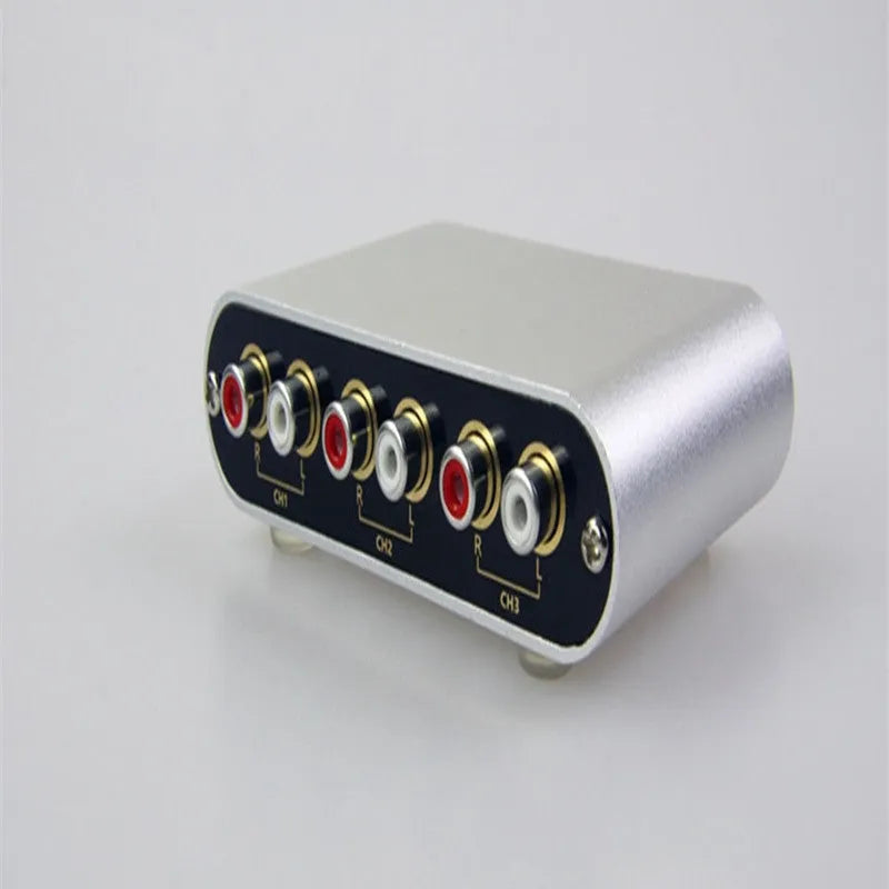 Silver aluminium audio source switch selector unit with infrared remote control on a black surface.