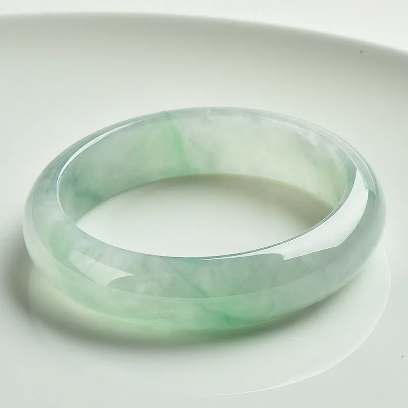 Light green solid jade bracelet on a wrist, showing its simple loop design and natural stone colour.