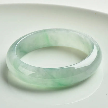 Light green solid jade bracelet on a wrist, showing its simple loop design and natural stone colour.