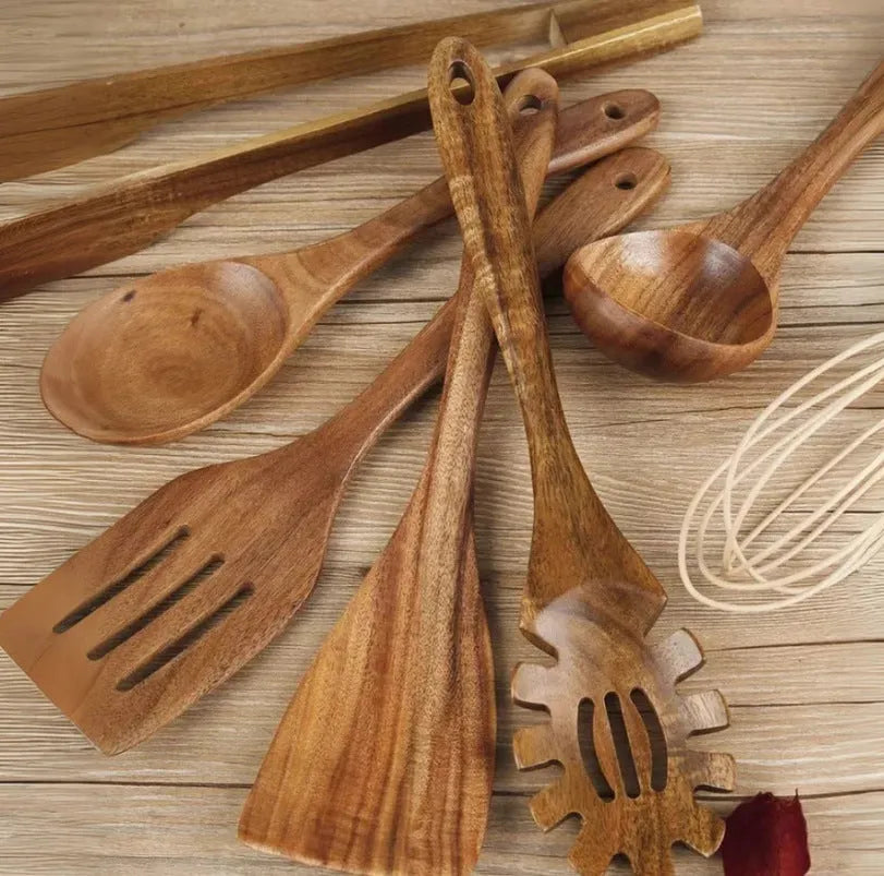 Set of seven light brown wooden cooking utensils including spoons, spatula, and turner on a kitchen counter.