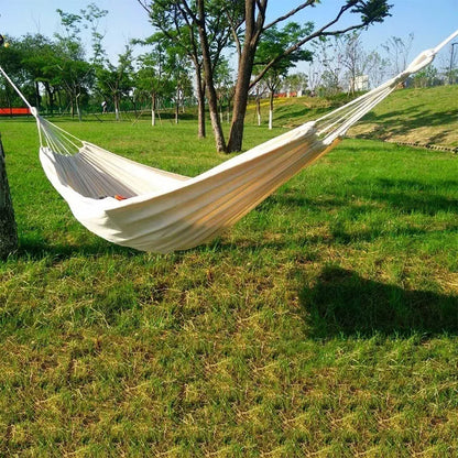 Cotton camping hammock with adjustable straps hanging between two trees in a forest