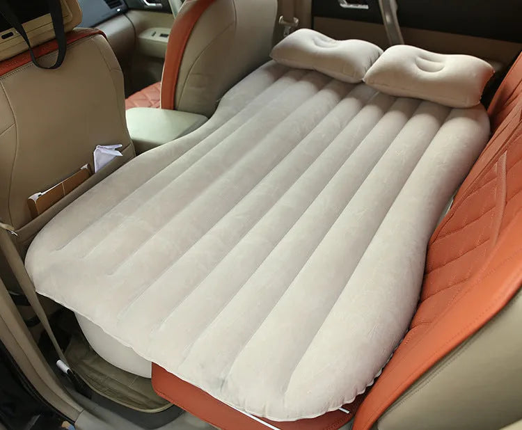 Black inflatable car bed with flocked surface and two pillows, shown folded into a chair inside a vehicle.