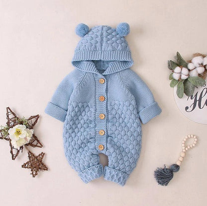 Baby wearing light blue knitted romper with hood and sleeveless design, single-breasted closure visible