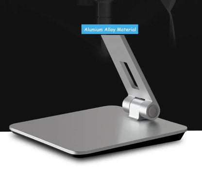 Silver foldable aluminium phone and tablet holder on a wooden desk, showing 360-degree rotation and silicone pads.