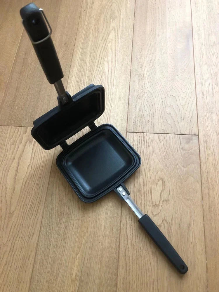 Black double-sided sandwich frying pan with heat-proof handle on stovetop