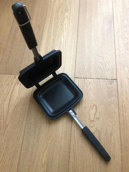 Black double-sided sandwich frying pan with heat-proof handle on stovetop