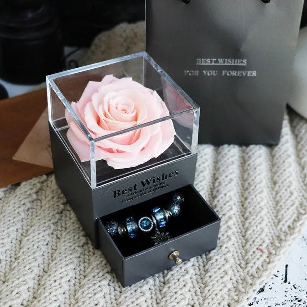 Blue and pink eternal flower gift box with roses and carnations on a table.