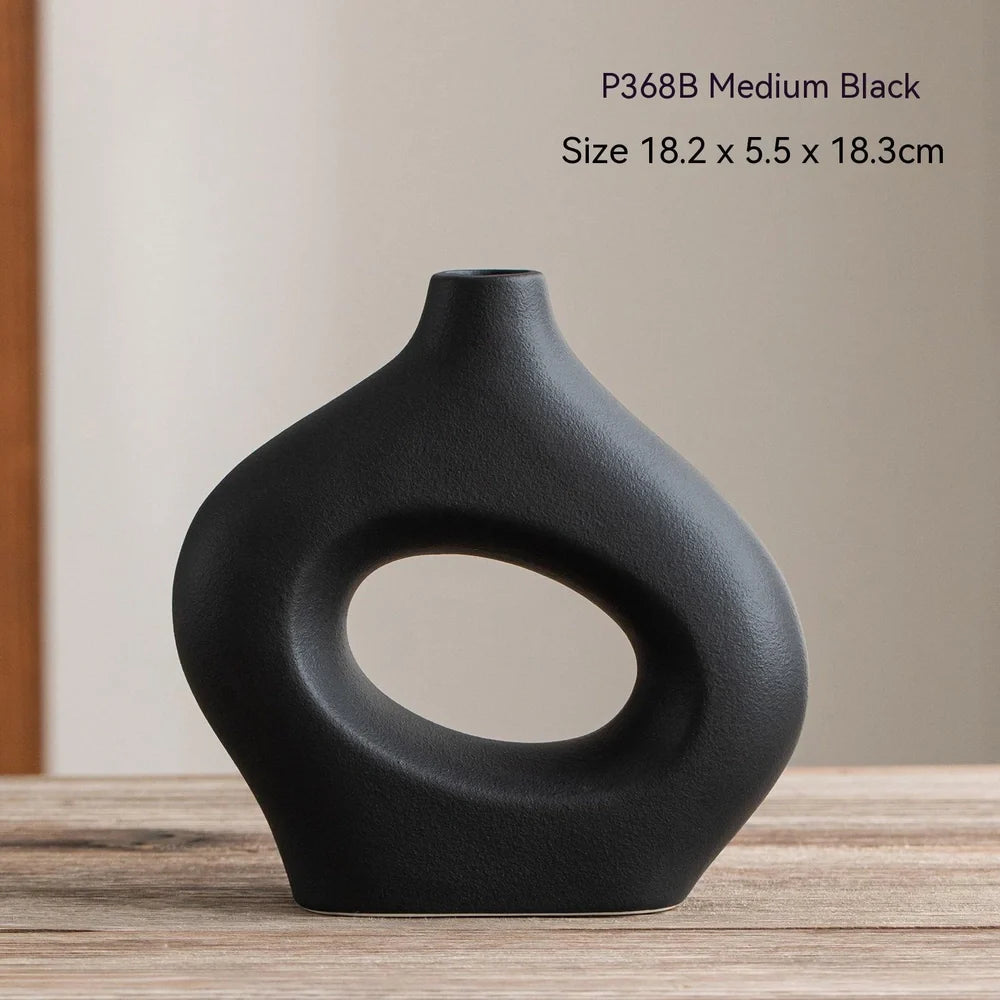 White ceramic circle vase with hand-painted coloured glaze on wooden table with dried flowers