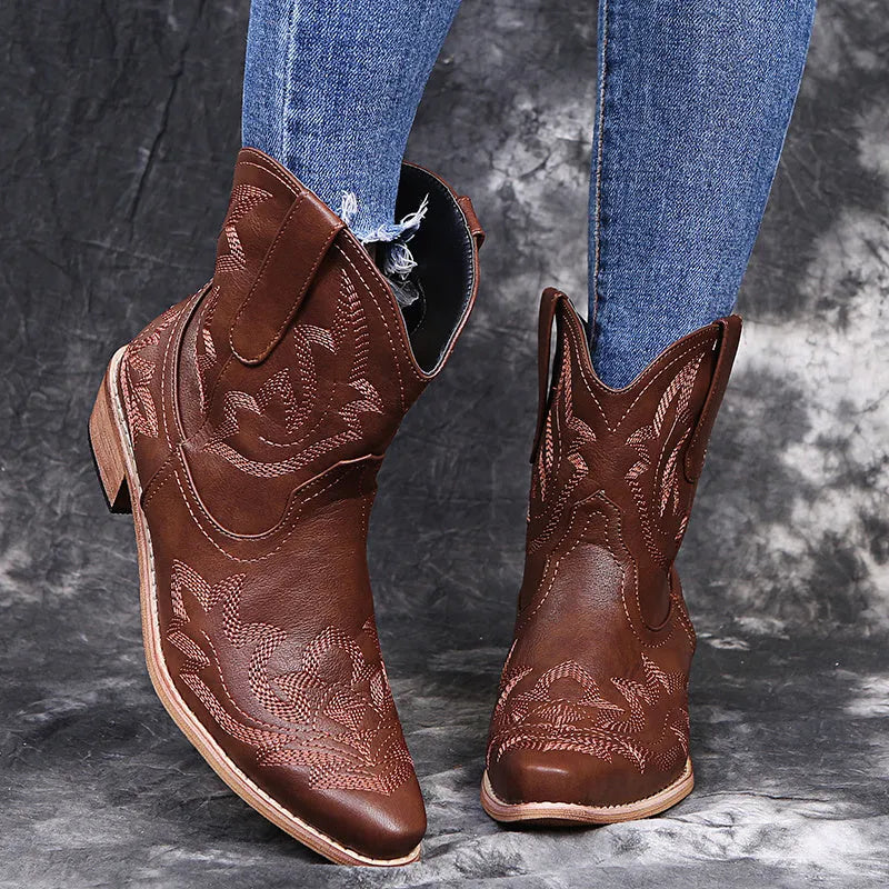 Women's blue embroidered cowboy ankle boots with a low wedge heel and pointed toe on a wooden floor.