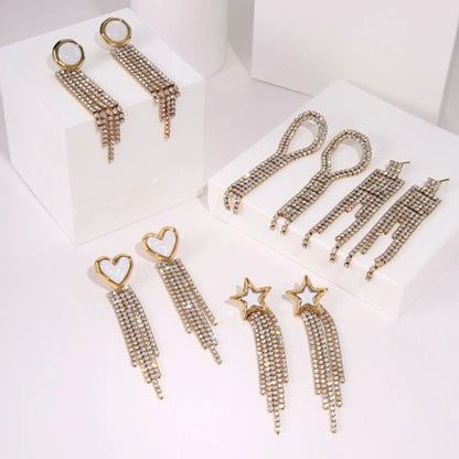 Gold-coloured women's earrings with a love heart shape, star details and dangling diamond-style tassels on a white background.