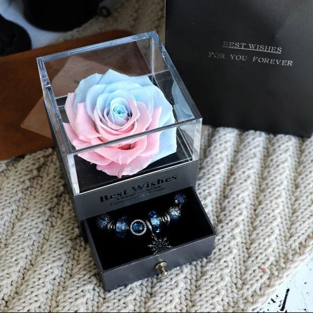 Blue and pink eternal flower gift box with roses and carnations on a table.