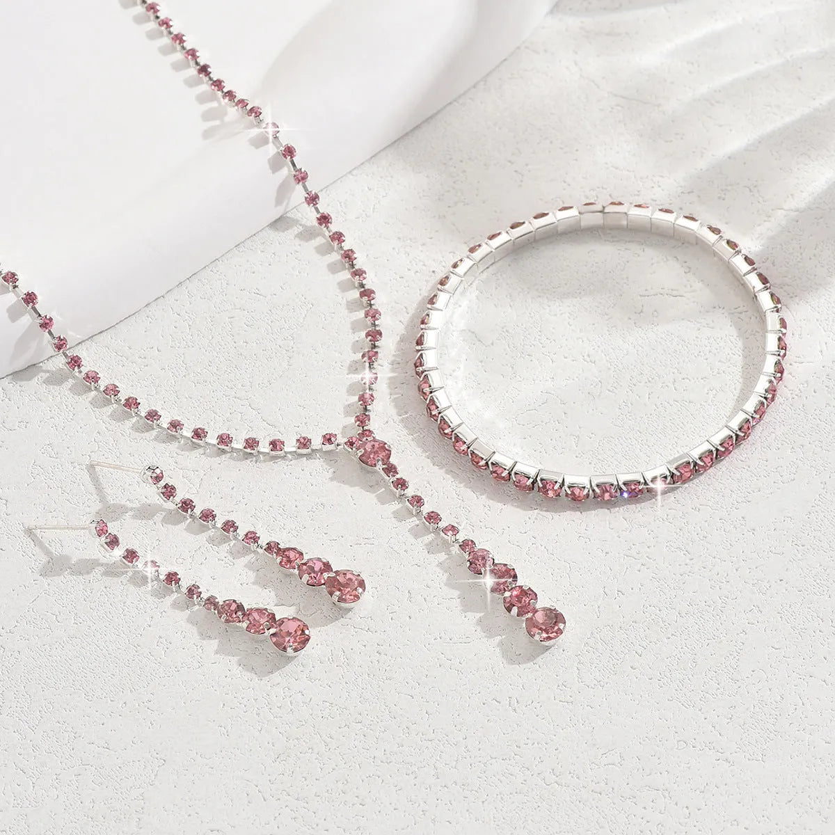 Women's silver pink rhinestone heart tassel earrings, necklace, and bracelet jewellery set on a white background.