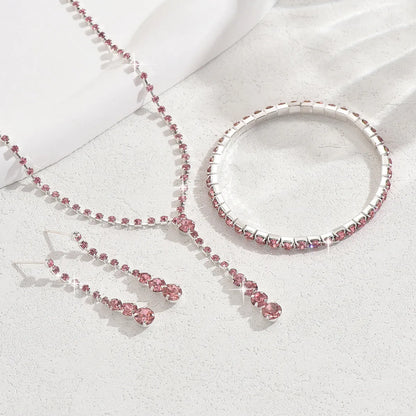 Women's silver pink rhinestone heart tassel earrings, necklace, and bracelet jewellery set on a white background.