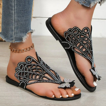 Women's black slip-on flip-toe sandals with rhinestone accents and hollow flat-heeled design on a light background