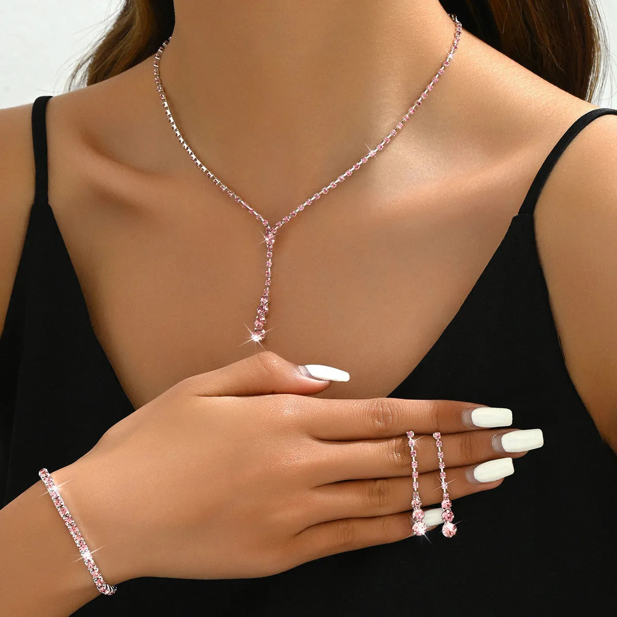Women's silver pink rhinestone heart tassel earrings, necklace, and bracelet jewellery set on a white background.