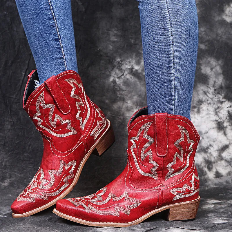 Women's blue embroidered cowboy boots with a low wedge heel and pointed toe on a wooden floor.