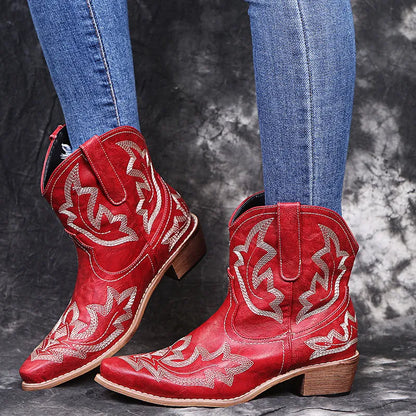 Women's blue embroidered cowboy ankle boots with a low wedge heel and pointed toe on a wooden floor.