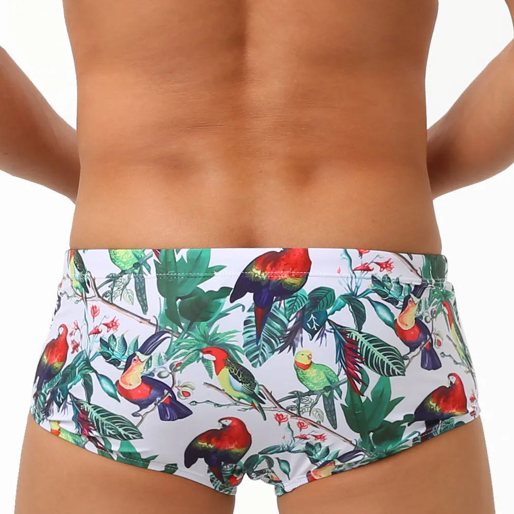 Men's blue swimming trunks with a detailed floral and bird print pattern, shown in a brief style.