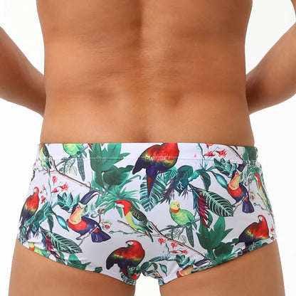 Men's blue swimming trunks with a detailed floral and bird print pattern, shown in a brief style.