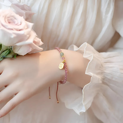 A hand-woven red rope bracelet with a strawberry quartz or garnet crystal, shown in simple styling.