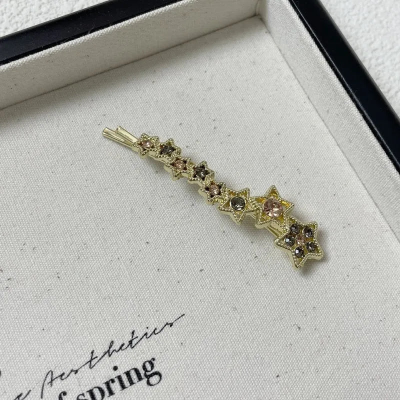 Gold electroplated hair barrette with a rhinestone five-pointed star, broken clip style for bangs.