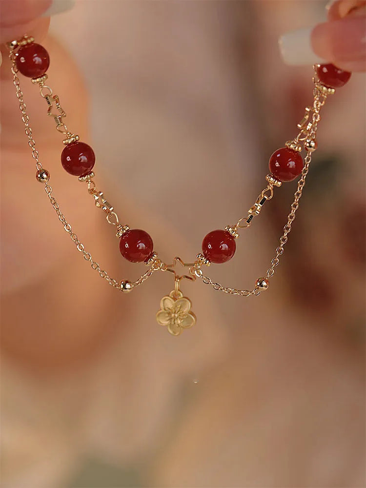 Red agate double layer bracelet with flower and peach blossom charms on a wrist.
