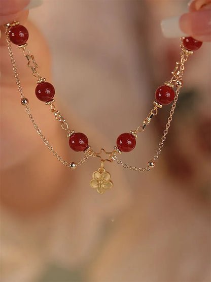 Red agate double layer bracelet with flower and peach blossom charms on a wrist.