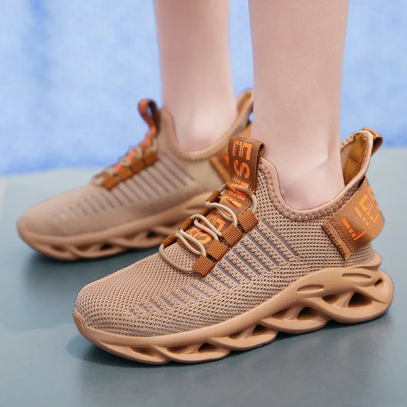 Children's black fabric sneakers with a Velcro strap and patterned EVA sole on a wooden floor.