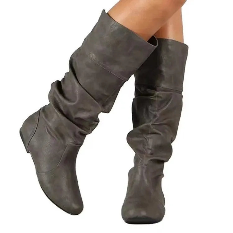 Women's flat slip-on boots in black with round toe and high cylinder shaft on a neutral background.