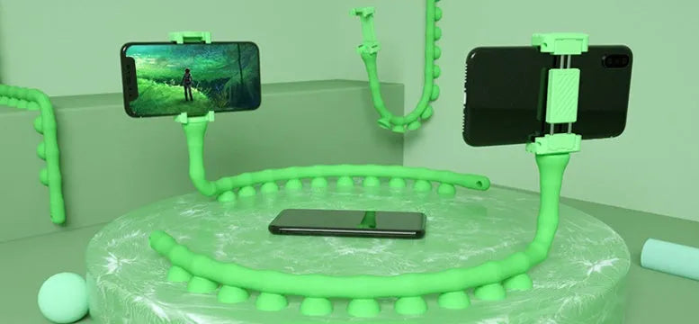 Black flexible gooseneck phone holder with suction cup mounted on a desk, holding a mobile phone at an angle.