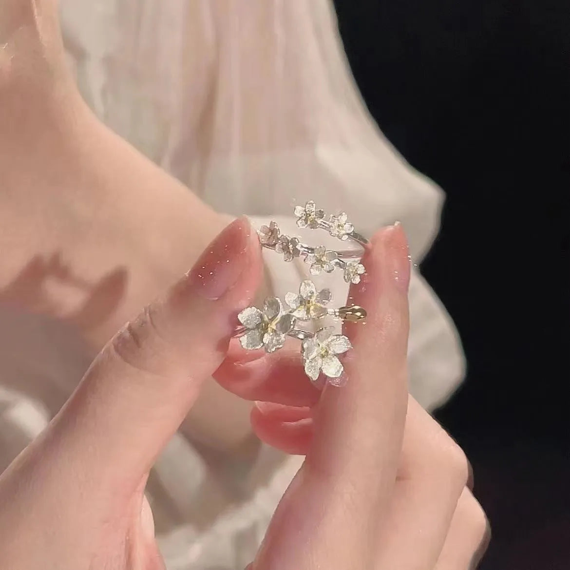 Adjustable three-dimensional jasmine flower ring in zinc alloy with electroplated finish on a hand.